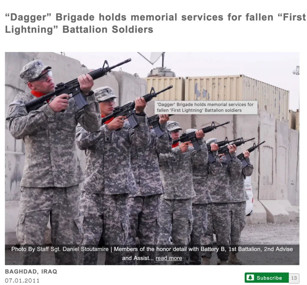An honor detail of five soldiers in camouflage uniforms stands in a line, firing a ceremonial volley with rifles during a memorial service. They are positioned against a backdrop of concrete barriers in Baghdad, Iraq. A text overlay at the bottom credits the photo to Staff Sgt. Daniel Stoutamire and identifies the group as members of Battery B, 1st Battalion.