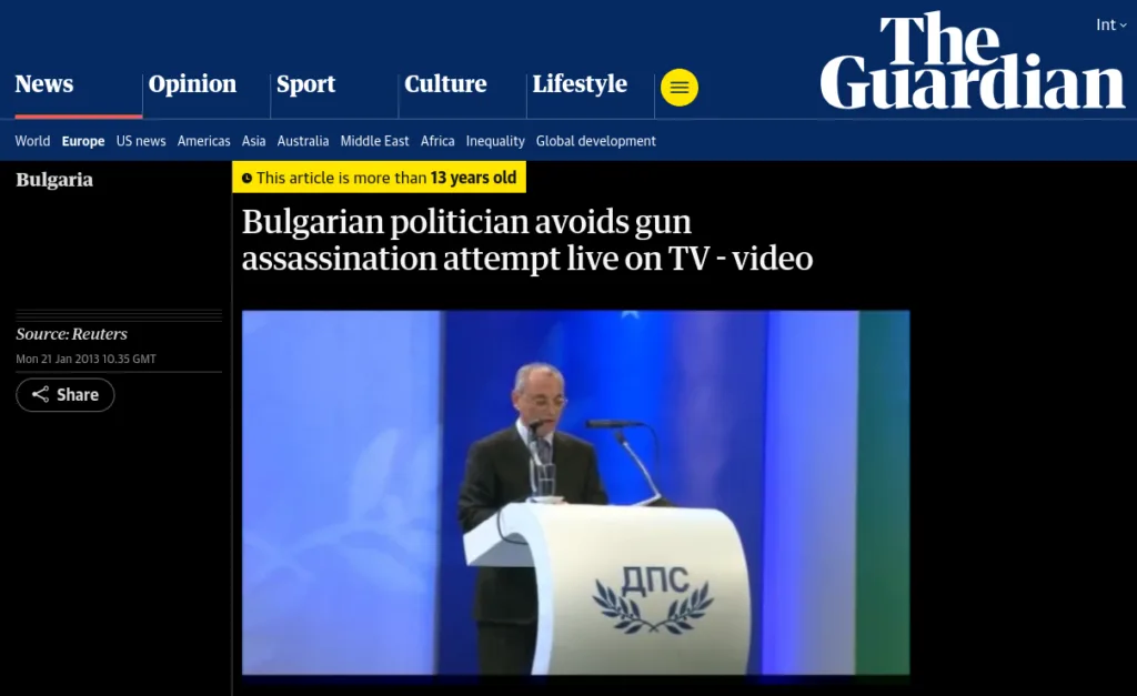 Screenshot of a Guardian article titled “Bulgarian politician avoids gun assassination attempt live on TV – video,” dated January 21, 2013. The image shows a man pointing a gun at Ahmed Dogan, leader of Bulgaria’s Movement for Rights and Freedoms party, during a televised speech. The podium displays Cyrillic letters “ДПС.” The caption explains Dogan escaped the attempt and the assailant carried knives.