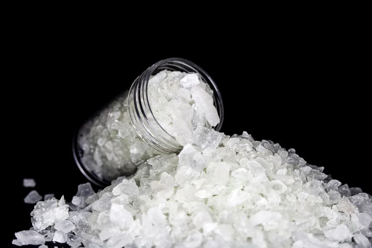 White MDMA crystals spilling from a glass jar representing the rise of chemical drug abuse among youth in Kerala.