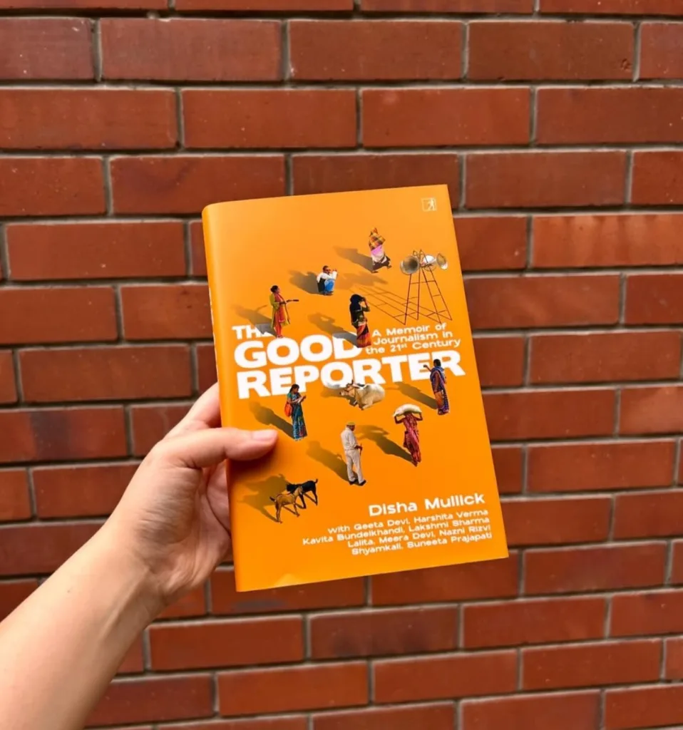 A hand holding a copy of The Good Reporter book cover against a red brick wall.